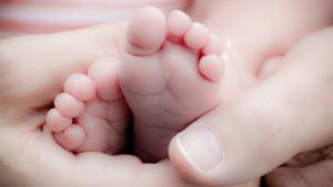Close-up of an adult's hands gently cradling a newborn baby's feet, symbolizing new life and care.