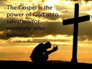 Silhouette of a person kneeling before a cross at sunset with text: “The Gospel is the power of God unto salvation for everyone who believes.”