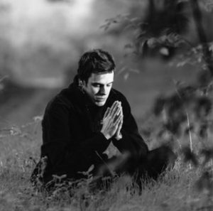 A person sitting peacefully outdoors with clasped hands, symbolizing prayer and spiritual reflection.