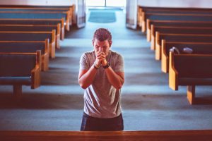 Young man praying alone in an empty church sanctuary, symbolizing personal struggle and spiritual seeking.